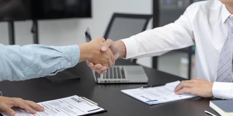 Geschäftlicher Handschlag am Schreibtisch mit Laptop und Dokumenten als Symbol für erfolgreichen Start und strukturiertes Onboarding.