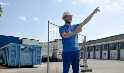 Ingenieur auf Baustelle koordiniert Subunternehmer per Smartphone und zeigt auf nächste Arbeitsetappe